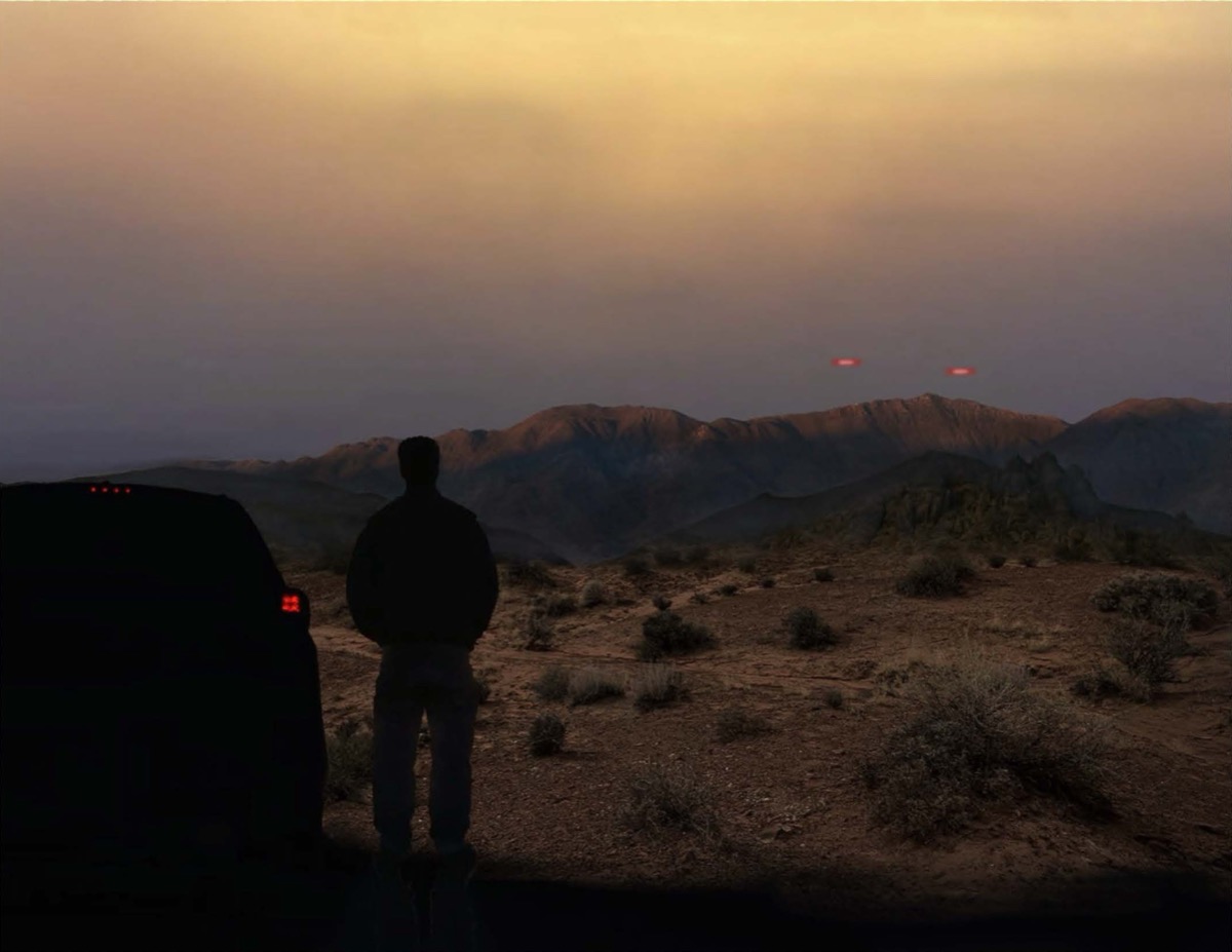 Una representación digital de una persona parada junto a un vehículo, mirando dos luces rojas en el cielo sobre un paisaje montañoso.